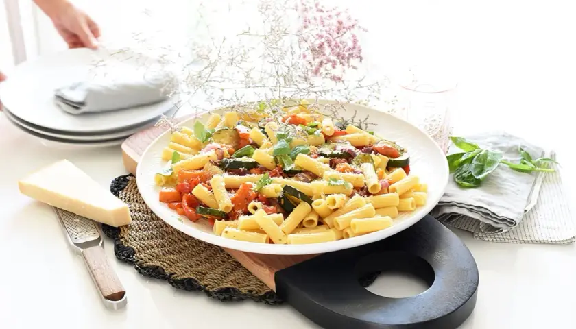 Plato de pasta con verduras salteadas, calabacín, tomate y albahaca, con queso parmesano rallado.