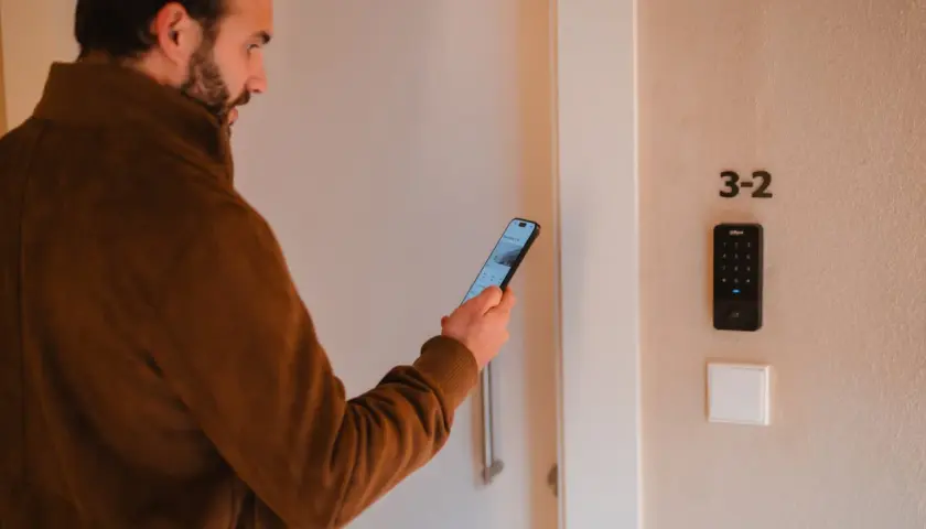Hombre con móvil frente a puerta con teclado numérico. Una de las desventajas de la domótica es la dependencia tecnológica.