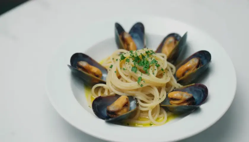 Spaghetti z małżami, danie pełne smaku morza, ozdobione świeżą natką pietruszki.