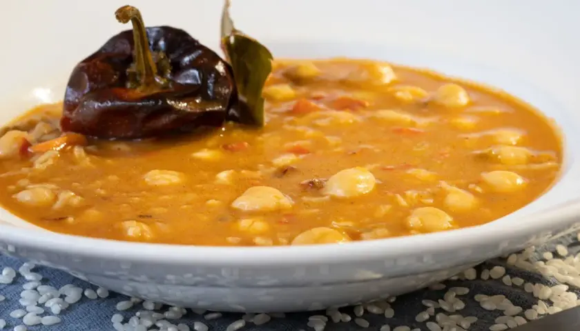 Un plato de garbanzos con arroz, con un pimiento seco y una hoja de laurel encima.