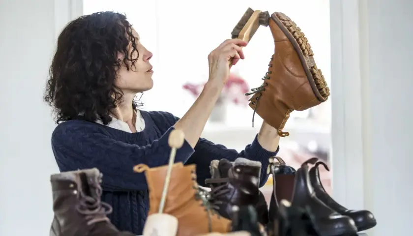 Une femme aux cheveux bouclés brosse une botte en cuir. Elle s'assure de la bonne fréquence de cirage de ses chaussures pour les garder en parfait état.