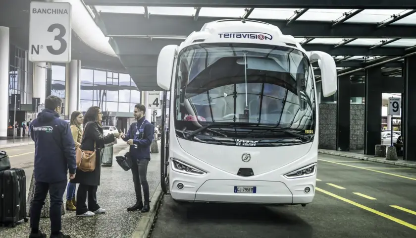 Autobus Terravision czeka na pasażerów na jednym z mediolan lotniska. Ludzie z bagażami rozmawiają z pracownikiem.