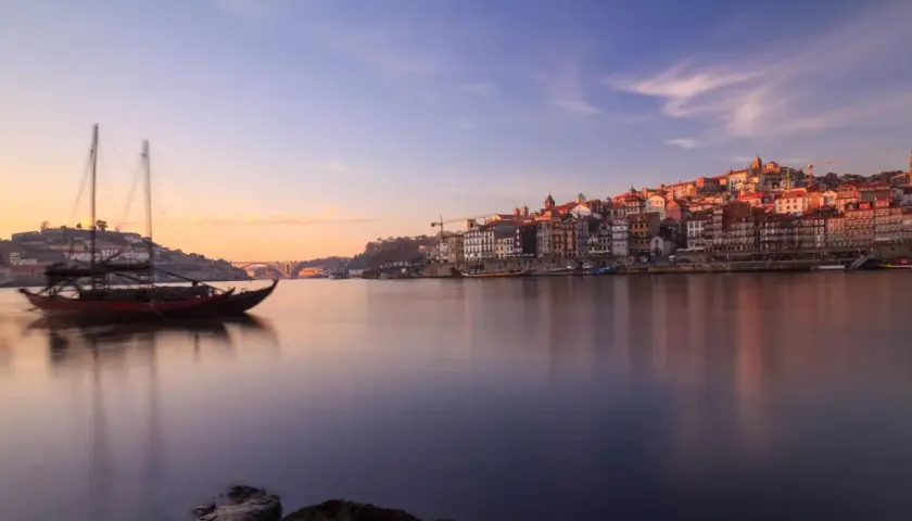 Barcos tradicionales navegan por el río Duero al amanecer, con la pintoresca ciudad de Oporto al fondo. Un lugar imprescindible que ver en el norte de Portugal.