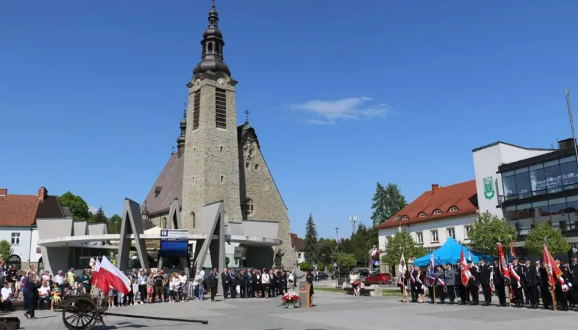 Uroczystość przed kościołem w Limanowej. Ludzie, delegacje w mundurach i polskie flagi.