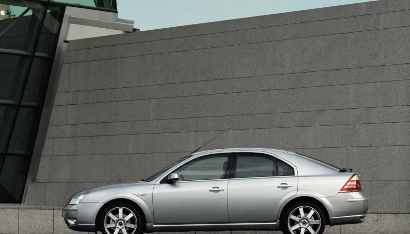 Srebrny Ford Mondeo MK3 2.0 TDCI stoi na tle nowoczesnego budynku z kamienną fasadą.