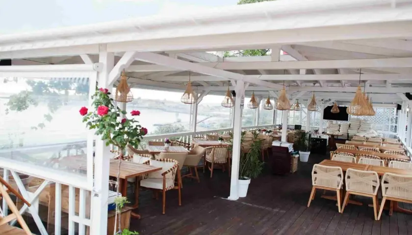 Letnia restauracja z widokiem na wodę. Krzesła i stoły z rattanu, wiszące lampy. Idealne miejsce na pyszne jurata jedzenie.
