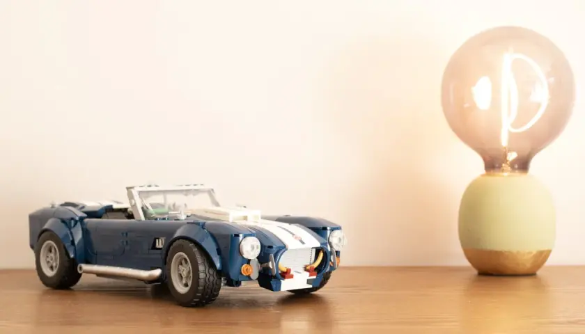 Ein blauer Lego Shelby Cobra steht neben einer leuchtenden Glühbirne.