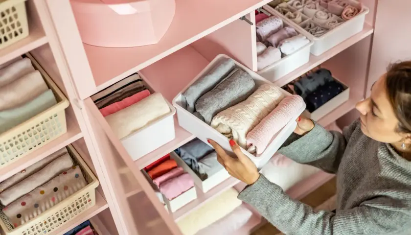 Frau sortiert Kleidung in einem rosa Kleiderschrank. So organisiere ich meinen Kleiderschrank: gefaltete Pullover und Socken in Behältern.