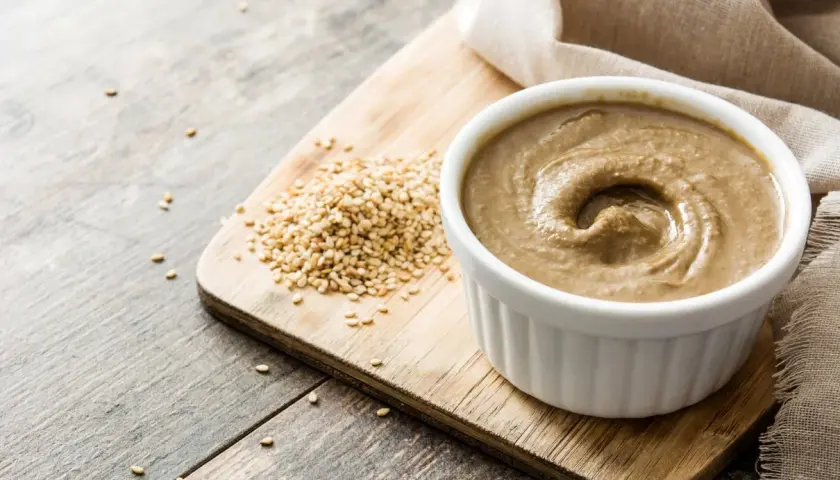 Domowe tahini jak zrobić? Ziarna sezamu i gotowa pasta na desce.