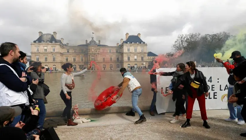 Protestujący z racami i dmuchanym obiektem przed budynkiem w Paryżu.