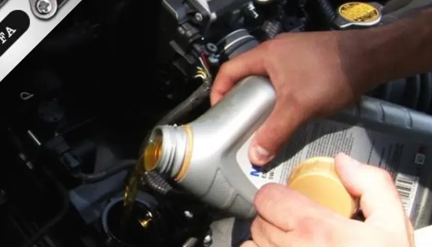 Mano che versa olio motore nel vano del motore. Il tappo giallo indica dove si mette l'olio motore.