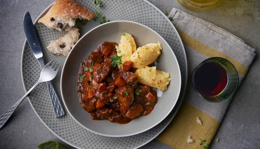 Herzhaftes Spezzatino di manzo mit cremigem Polenta, dazu ein Glas Rotwein und rustikales Brot.