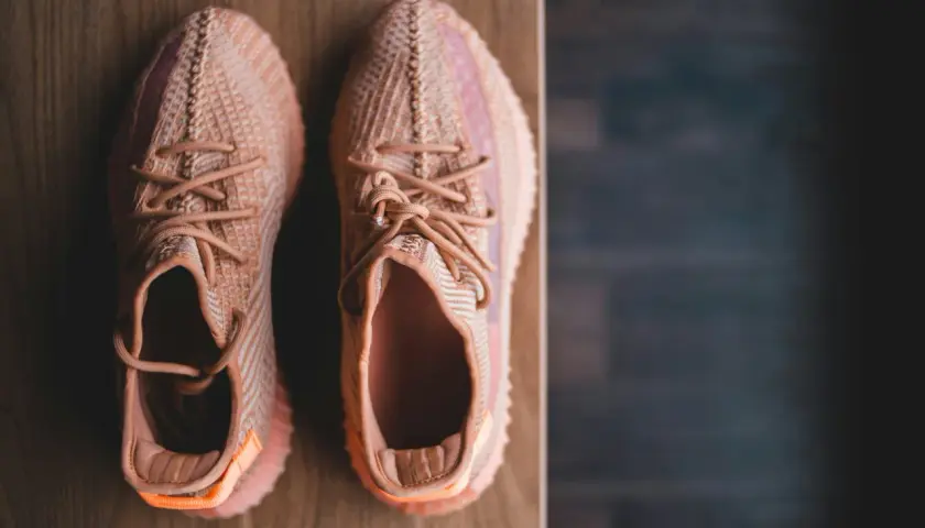 Pomarańczowe sneakersy z plecionki, idealne na szeroką stopę, leżą na drewnianym blacie.