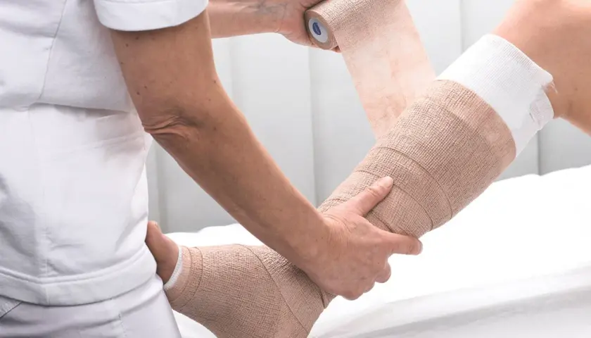 Eine Person wickelt einen Verband um ein Bein zur Kompression.