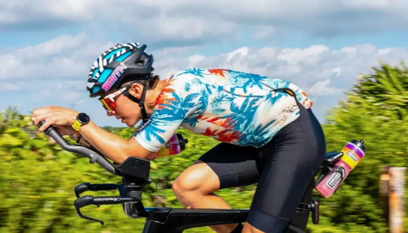 Ciclista en Mallorca en bici, con casco y gafas, pedaleando con fuerza en un día soleado.