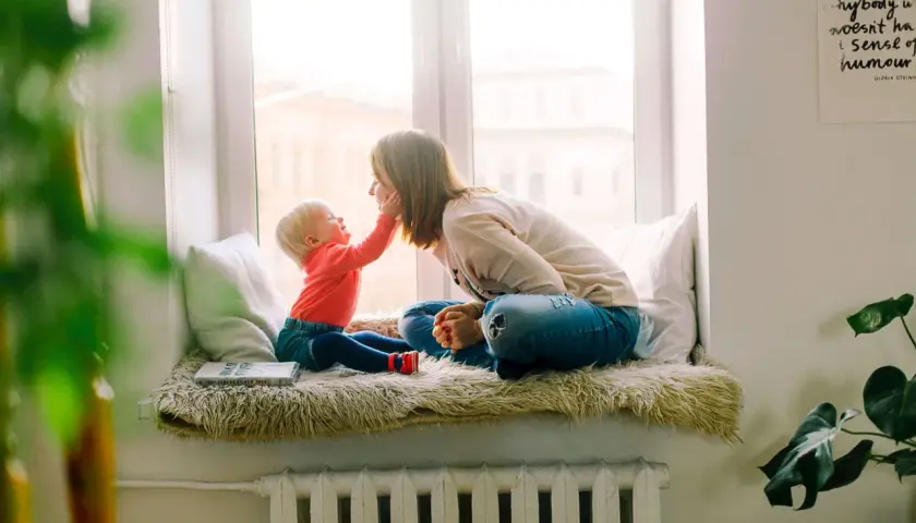 Mama i dziecko siedzą na parapecie. Wzór umowy najmu mieszkania dla rodziny z dzieckiem jest na książce.