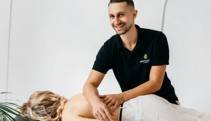 Uśmiechnięty masażysta wykonuje masaż klasyczny pleców. Uczy się technik na kursie masażu.