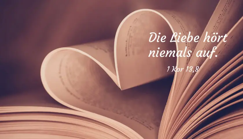 Ein aufgeschlagenes Buch formt ein Herz. Darauf steht: "Die Liebe hört niemals auf. 1 Kor 13,8". Bibelverse über die Liebe für Partner.