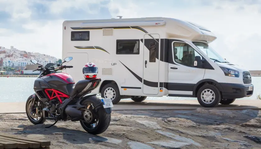 Un camping-car et une moto sportive Ducati sont garés près de la mer, prêts pour une aventure.