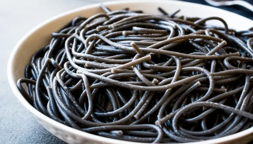 Czarny makaron spaghetti w białej misce, zbliżenie.