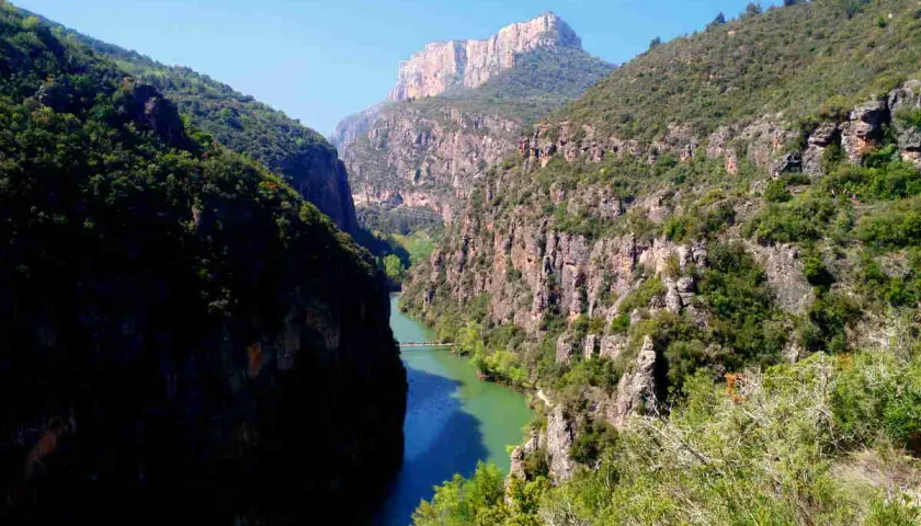 El río serpentea entre imponentes paredes rocosas en el congost del Mu, coronado por un pico montañoso.