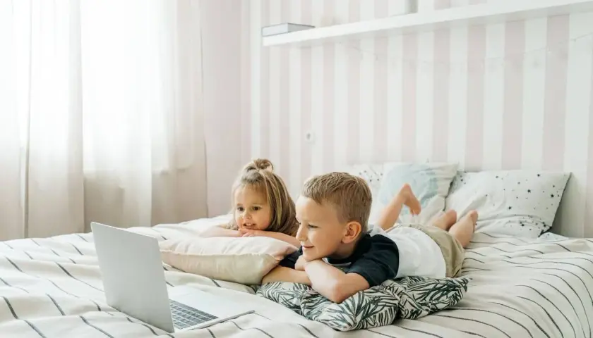 Dzieci leżą na łóżku, oglądając edukacyjne bajki dla dzieci na laptopie.