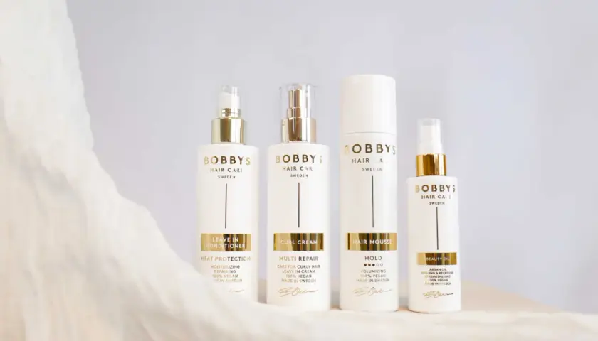Fyra vita flaskor med guldfärgade detaljer från Bobby's Hair Care. En huskur mot statiskt hår.