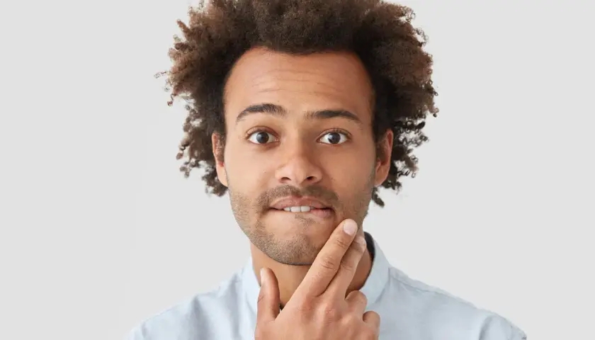 Uomo con capelli ricci e barba corta, con un dito sul mento, espressione pensierosa, come se avesse un sapore acido in bocca.