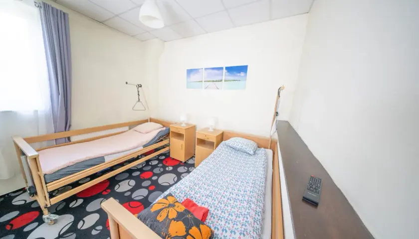 Pokój z dwoma łóżkami, szafkami nocnymi i kolorowym dywanem.