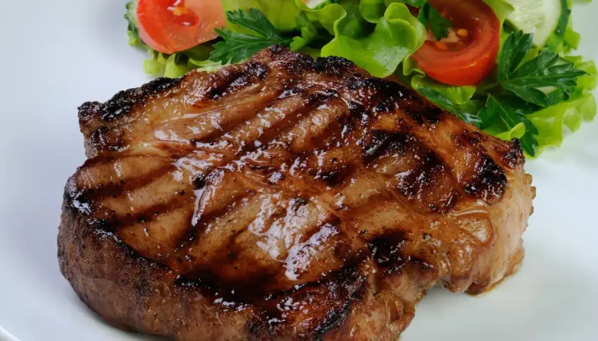 Bistecca di maiale succulenta e grigliata, servita con un'insalata fresca di lattuga, pomodoro e cetriolo.