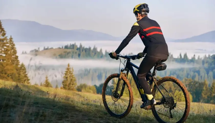 Rowerzysta w kasku i sportowym stroju pokonuje górski szlak. Jego rytmiczna kadencja i błotniste opony świadczą o trudnej trasie.