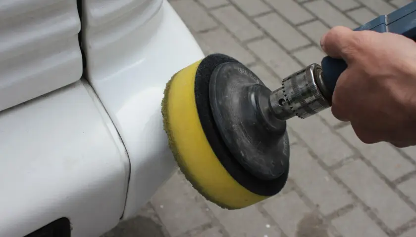 Dłoń trzyma polerkę z żółtą gąbką, polerując biały lakier samochodu.