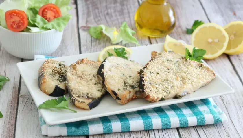 Fette di pesce spada impanate con sesamo, cotte in friggitrice ad aria, servite con limone e insalata.