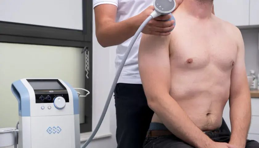 Fizjoterapeuta stosuje aparat do terapii falą uderzeniową na bark pacjenta, co może pomóc w leczeniu zapalenia kaletki podbarkowej domowe sposoby.