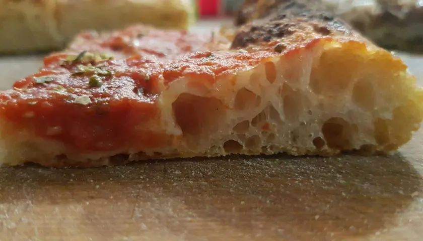 Fetta di pizza con pomodoro e erbe, la sua alveolatura mostra una perfetta pizza lievitazione 24 ore.
