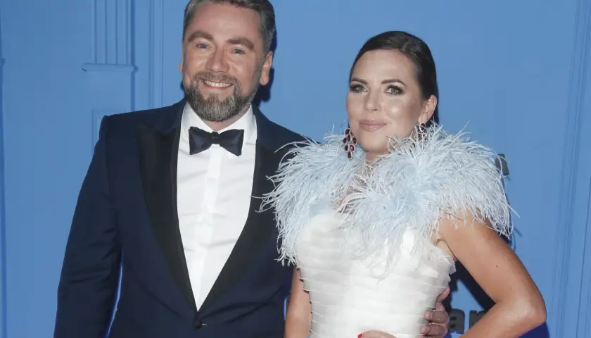 Mąż Oli Kwaśniewskiej, Piotr, w eleganckim smokingu u boku żony w białej sukni z piórami.