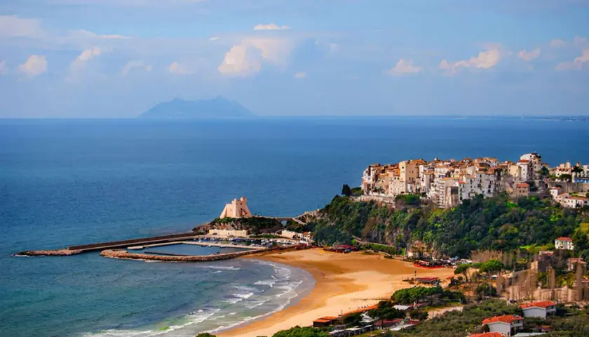 Vue d'un village pittoresque perché sur une falaise surplombant la mer, avec une plage de sable et un port. On dirait un **ostie** de **Rome** !