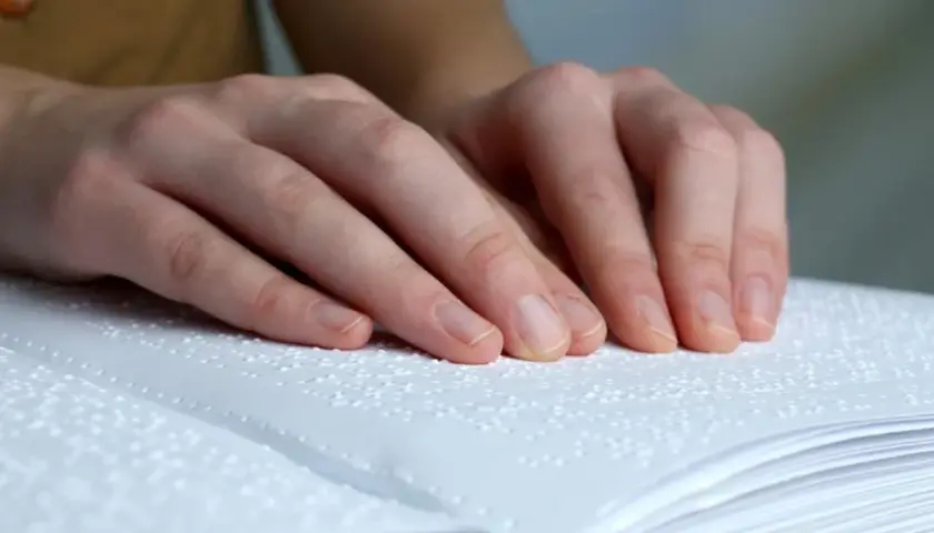 Dłonie osoby czytającej książkę w alfabecie Braille'a.