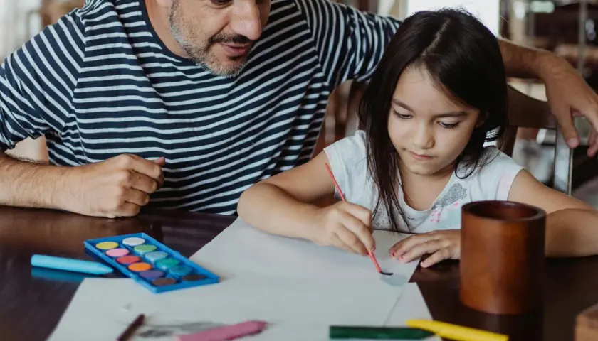 Padre e hija pintando con acuarelas y lápices de colores. Un momento de creatividad con materiales de escuela infantil.