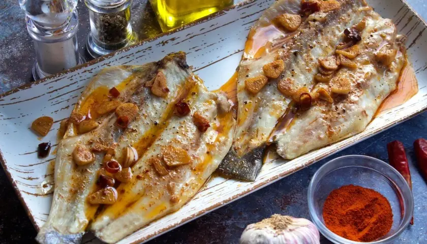 Dos filetes de lubina a la bilbaina, dorados y jugosos, con láminas de ajo y guindilla, listos para disfrutar.