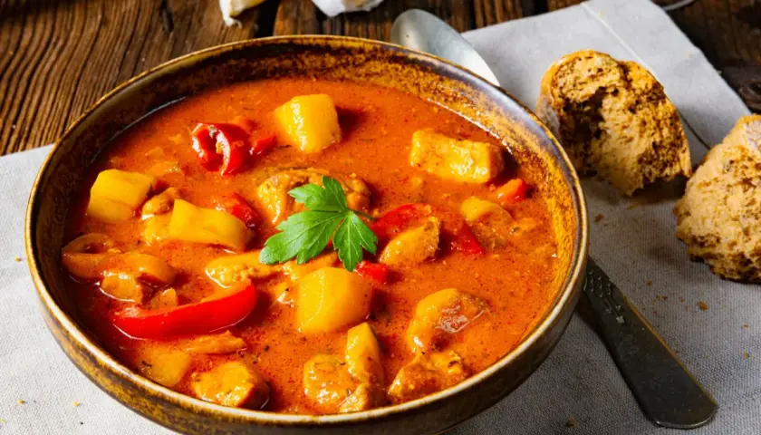 Gęsta, aromatyczna zupa gulaszowa przepis babci, z kawałkami mięsa, ziemniaków i papryki, podana w glinianej misce z chlebem.