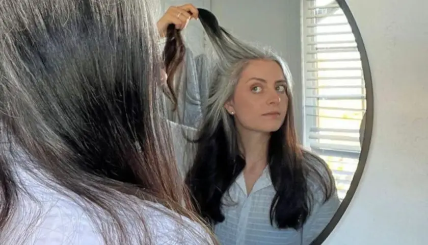 Mujer se mira al espejo, su cabello es una mezcla de negro y canas amarillas, un estilo natural y único.
