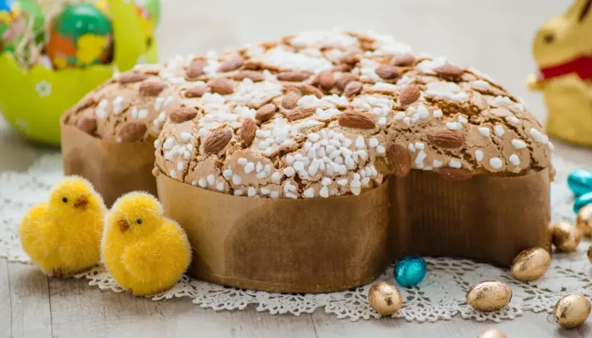 Colomba pasquale, un classico tra i dessert pasquali, decorata con mandorle e zuccherini, circondata da pulcini e uova di cioccolato.