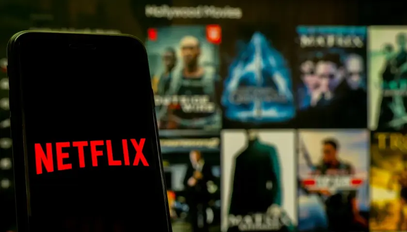 Telefon z logo Netflix na tle ekranu z filmami. Zastanawiasz się, co obejrzeć na Netflixie?