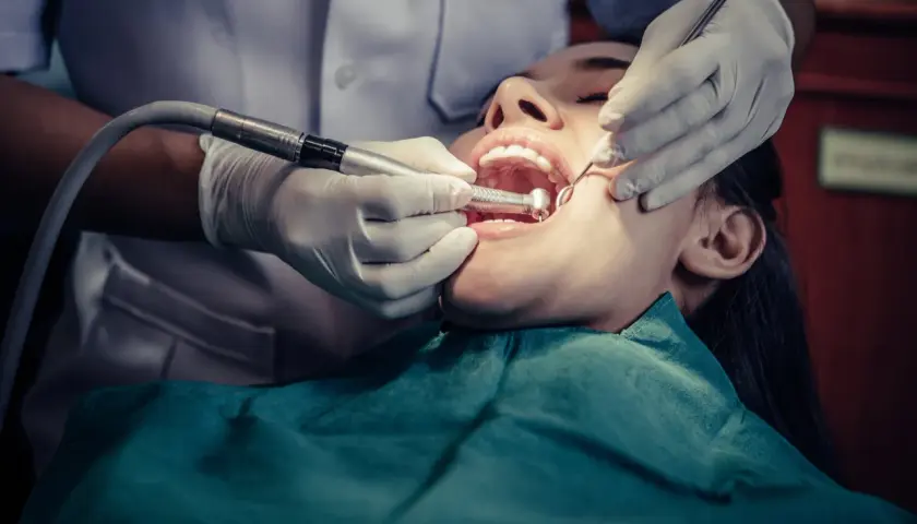 Dentista trabajando en la boca de una paciente, realizando una **conclusión dental** con instrumental y pieza de mano.