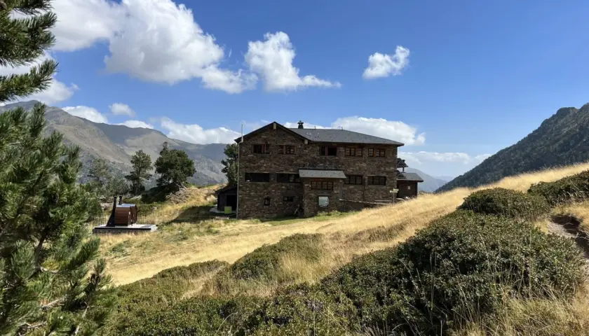 Refugio Comapedrosa, un edificio de piedra en un paisaje montañoso con hierba seca y cielo azul.