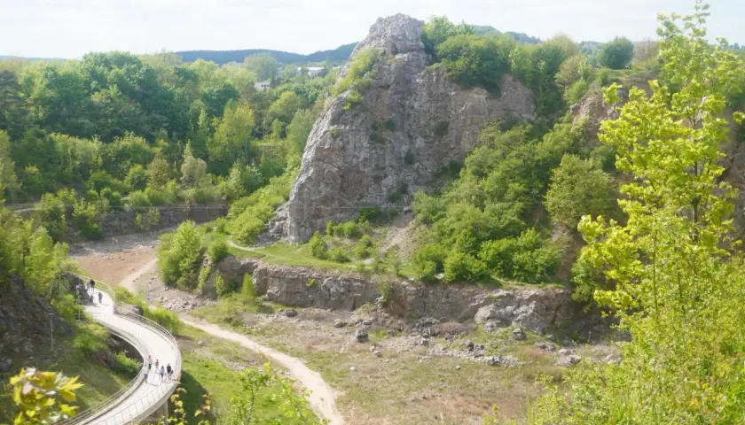 Kamieniołom w Kielcach z krętą ścieżką i grupą spacerowiczów. W oddali skaliste góry porośnięte zielenią.