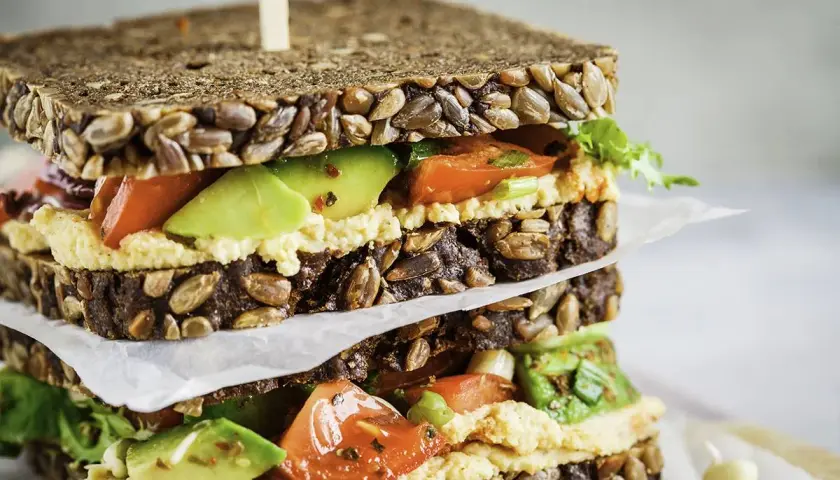 Delicioso sandwich de hummus con aguacate, tomate y pan integral con semillas.