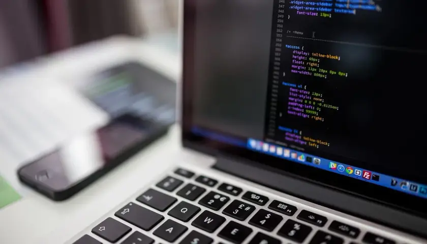 Laptop z kodem na ekranie, obok smartfon. Szukasz sposobu, jak przyspieszyć procesor w laptopie?