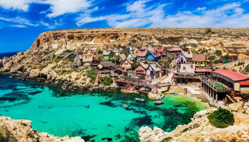 Bunte Häuser am malta beach, umgeben von Felsen und türkisfarbenem Wasser. Boote schaukeln sanft in der Bucht.